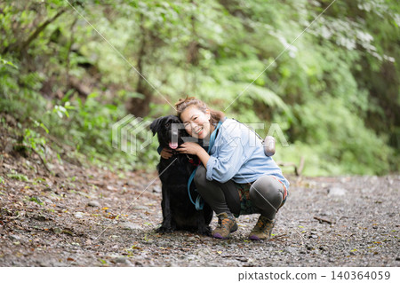 A woman smiles as she interacts with her dog in the forest, enjoying her outdoor lifestyle – a direct look at the camera. 140364059
