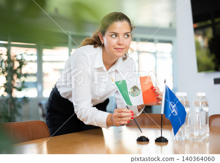 Preparing for business negotiations - woman sets small flags of countries of Mexico and NATO (OTAN) on table 140364060