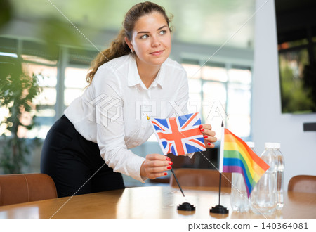Young woman putting UK and LGBT flags on table in office Young woman putting UK and LGBT flags on table in office 140364081