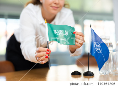 Female secretary places flags of the NATO (OTAN) and Saudi Arabia on the table before negotiations of top political figures Female secretary places flags of the NATO (OTAN) and Saudi Arabia on the table before negotiations of top political figures 140364206