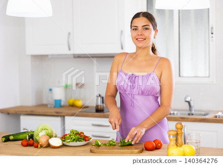 Cheerful girl in nightwear preparing salad at home Cheerful girl in nightwear preparing salad at home 140364276
