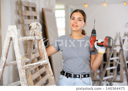 Smiling woman holding drill, repair works in apartment Smiling woman holding drill, repair works in apartment 140364475