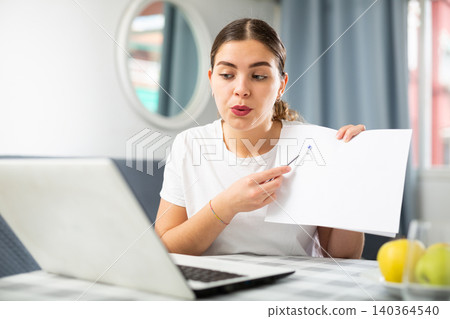 Young woman communicates via video link, showing something on paper Young woman communicates via video link, showing something on paper 140364540