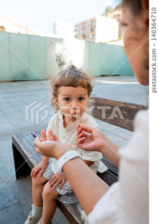 Caregiver Feeding Fresh Melon to Child on Bench Caregiver Feeding Fresh Melon to Child on Bench 140364710