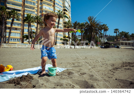 Happy Toddler Throwing Sand With Shovel on Beach Happy Toddler Throwing Sand With Shovel on Beach 140364742
