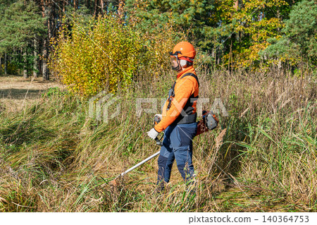 Brush cutter operator mowing weeds, grass in field, landscape maintenance and safety gear 140364753