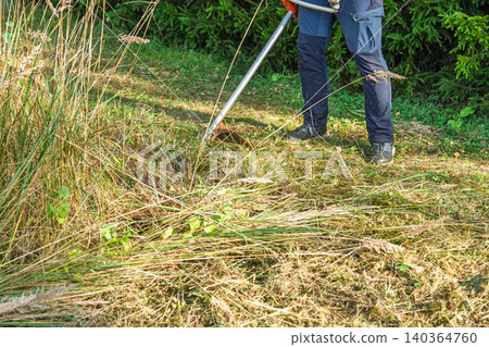 Mowing Tall Grass with String Trimmer in Summer, Landscaping and Yard Maintenance Concept Mowing Tall Grass with String Trimmer in Summer, Landscaping and Yard Maintenance Concept 140364760