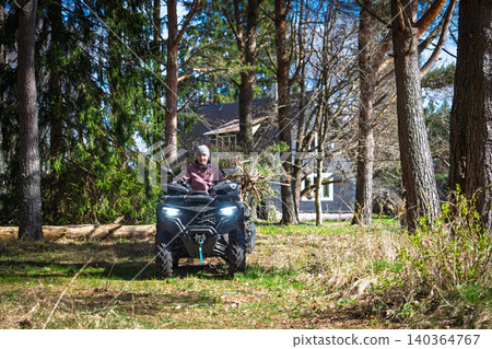 Woman riding an ATV quad bike through a forest, enjoying an outdoor adventure in Estonia 140364767