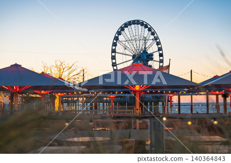 Scheveningen beach resort at sunset with Ferris wheel, umbrellas and coastal promenade in the H 140364843