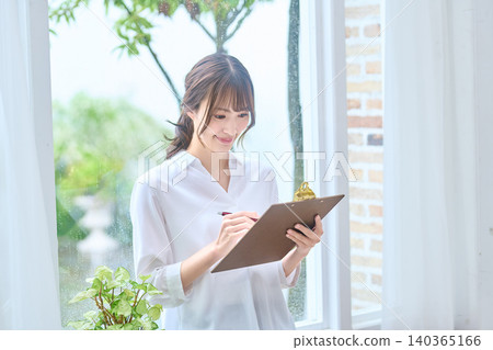 一位女士一邊在寫字板上寫字,一邊面帶微笑。 一位女士一邊在寫字板上寫字,一邊面帶微笑。 140365166