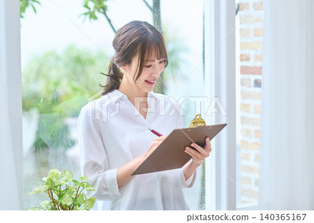 一位女商人一邊在寫字板上寫字,一邊微笑。 一位女商人一邊在寫字板上寫字,一邊微笑。 140365167