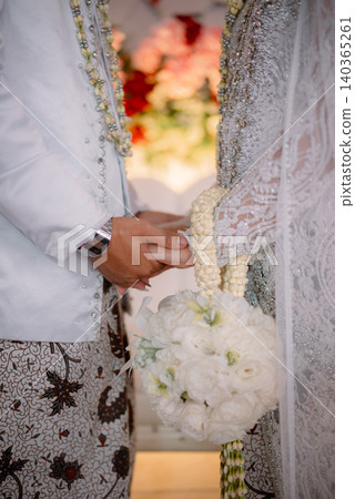A traditional Javanese bridal couple holding hands while holding a bouquet of white jasmine flowers. 140365261