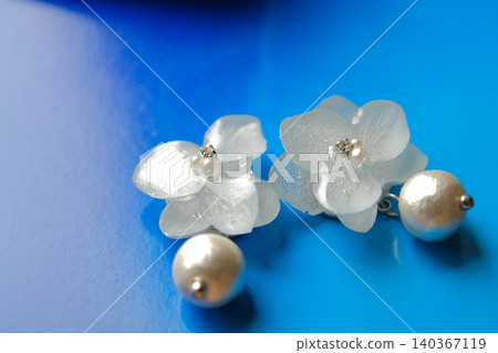 A pair of earrings featuring beautiful light blue hydrangeas against a deep blue background (horizontal composition). A pair of earrings featuring beautiful light blue hydrangeas against a deep blue background (horizontal composition). 140367119