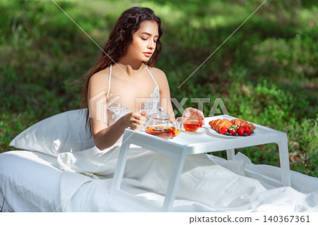 Young woman has breakfast in bed in a summer forest Young woman has breakfast in bed in a summer forest 140367361