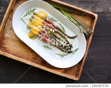 Roasted prosciutto wrapped asparagus with sauce on a white platter Roasted prosciutto wrapped asparagus with sauce on a white platter 140367576