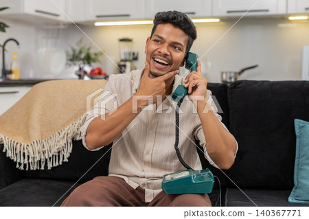 Indian man talks on retro corded phone nostalgic call listens and speaks with smile and gentle laugh Indian man talks on retro corded phone nostalgic call listens and speaks with smile and gentle laugh 140367771
