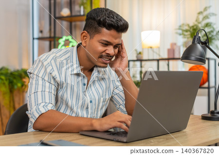 Indian man with laptop suffers headache rubs temples squints at screen needs rest break and relief Indian man with laptop suffers headache rubs temples squints at screen needs rest break and relief 140367820