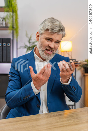 Middle-aged businessman argues on speakerphone smartphone angry gestures about shipping delay issues Middle-aged businessman argues on speakerphone smartphone angry gestures about shipping delay issues 140367869