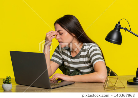 Woman tired rubbing eyes looking at laptop sitting at table after working late exhausted expression Woman tired rubbing eyes looking at laptop sitting at table after working late exhausted expression 140367968