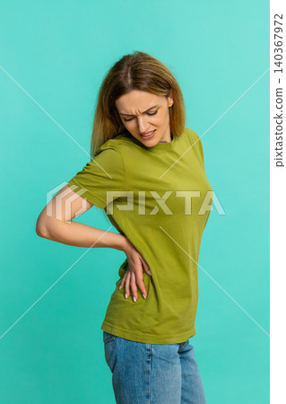 Woman holding lower back and straightening posture showing painful backache or spine muscle strain Woman holding lower back and straightening posture showing painful backache or spine muscle strain 140367972