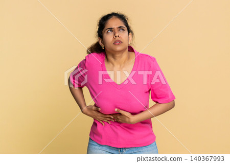 Indian woman bending forward holding stomach, face grimacing in severe pain expressing discomfort Indian woman bending forward holding stomach, face grimacing in severe pain expressing discomfort 140367993