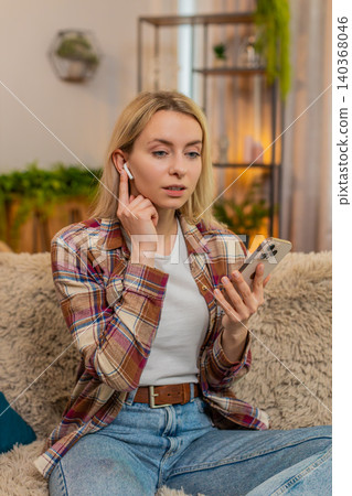 Adult woman listening to voice message with wireless earphones at home surprised by unexpected audio Adult woman listening to voice message with wireless earphones at home surprised by unexpected audio 140368046