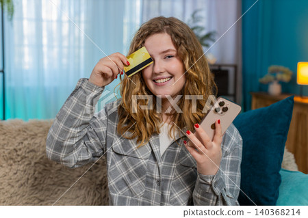 Young woman sitting on sofa holding bank card and smartphone making online payment or money transfer Young woman sitting on sofa holding bank card and smartphone making online payment or money transfer 140368214