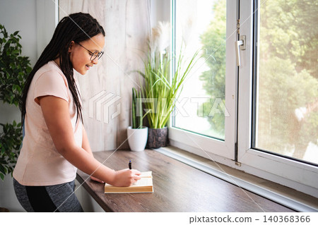 Teenager girl writing notes studying at home desk Teenager girl writing notes studying at home desk 140368366