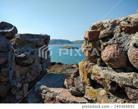 Scenic view of the blue sea and a small island through an ancient stone wall opening. Scenic view of the blue sea and a small island through an ancient stone wall opening. 140368692