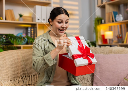 Young woman on home sofa opening gift box with joyful surprise and celebrating happy present at home Young woman on home sofa opening gift box with joyful surprise and celebrating happy present at home 140368699