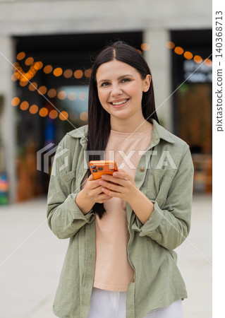 Young woman portrait with smartphone walking in city street smiling during travel chat app lifestyle Young woman portrait with smartphone walking in city street smiling during travel chat app lifestyle 140368713