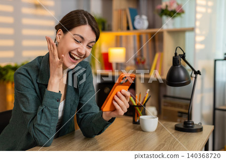 Young woman on home table celebrating success with smartphone happy winning news in cozy living room Young woman on home table celebrating success with smartphone happy winning news in cozy living room 140368720