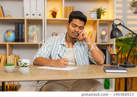 Indian man on home table writing shopping list on paper and planning home purchases with calm focus Indian man on home table writing shopping list on paper and planning home purchases with calm focus 140368913