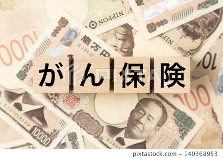 A block with "cancer insurance" written on it and lots of 10,000 yen bills. A block with "cancer insurance" written on it and lots of 10,000 yen bills. 140368953