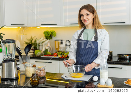 Middle-aged woman whisking eggs for omelet in home kitchen smiling for healthy diet nutrition plan Middle-aged woman whisking eggs for omelet in home kitchen smiling for healthy diet nutrition plan 140368955
