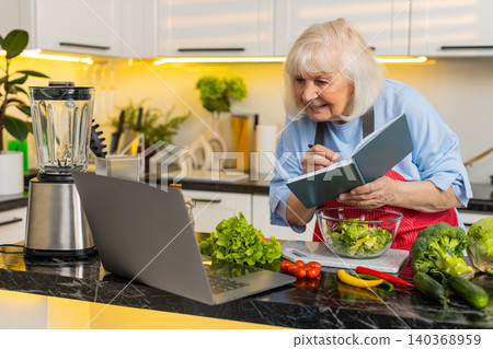 Senior old woman smiling with laptop and notebook planning healthy diet menu in modern home kitchen Senior old woman smiling with laptop and notebook planning healthy diet menu in modern home kitchen 140368959