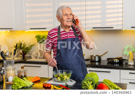 Senior old man mixing fresh salad in home kitchen while talking on smartphone for healthy diet plan Senior old man mixing fresh salad in home kitchen while talking on smartphone for healthy diet plan 140368961