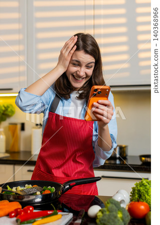 Young woman smiling using smartphone in home kitchen enjoying break during healthy meal prep routine 140368966