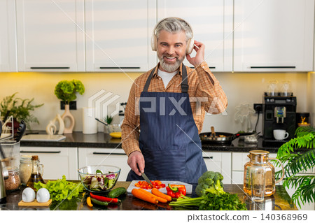 Middle-aged man chopping red pepper wearing headphones enjoying music while preparing healthy meal 140368969
