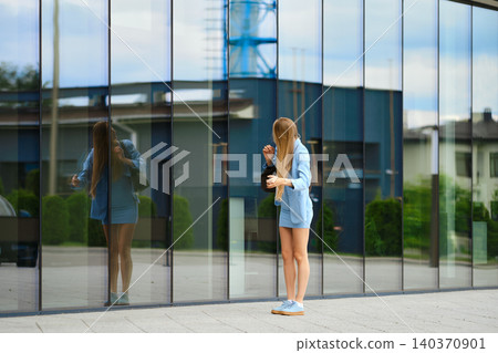 Woman with long blonde hair looking at her reflection in glass wall in urban area during afternoon 140370901