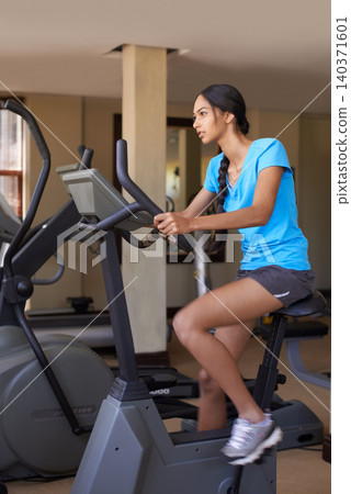 Woman, cardio and exercise bike in gym, active and stationary machine for workout at club. Female person, body health and cycling for strength training, challenge and equipment for fitness or action 140371601