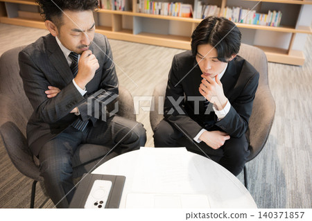 The image of a businessman's office with bookshelves, where they consult while looking at documents, and the image of a legal professional such as an administrative scrivener or other legal professional, including contracts. 140371857