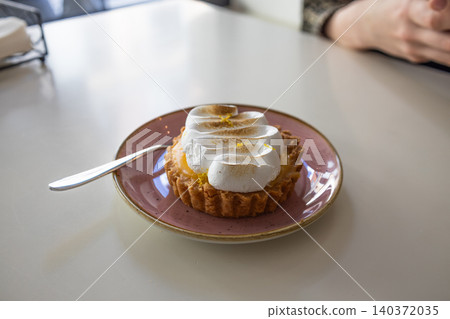 Lemon meringue tart on a pink plate with spoon Lemon meringue tart on a pink plate with spoon 140372035