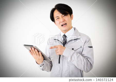 一位身穿灰色工作服的中年商人,在白色背景下看著平板電腦,神情沮喪。 一位身穿灰色工作服的中年商人,在白色背景下看著平板電腦,神情沮喪。 140372124