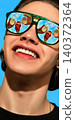 Smiling man in green sunglasses with raised cocktails reflected in lenses against blue sky 140372364