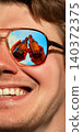 Close up man in sunglasses with beer bottles reflected in one lens against blue summer sky. 140372375