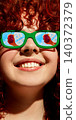 Close up red haired woman in green sunglasses with red drink reflected in lenses on blue sky 140372379