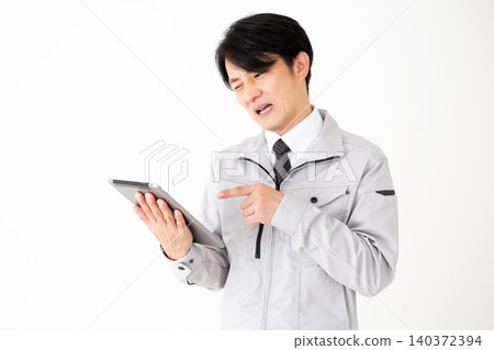 A middle-aged businessman in gray work clothes looks dejected while looking at a tablet against a white background. A middle-aged businessman in gray work clothes looks dejected while looking at a tablet against a white background. 140372394