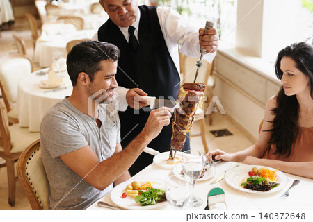 Happy couple, date and waiter with kebab for serving, fine dinning or romantic dinner at table. Young man and woman with chef cutting skewer of food for meal, eating or enjoying service at restaurant 140372648