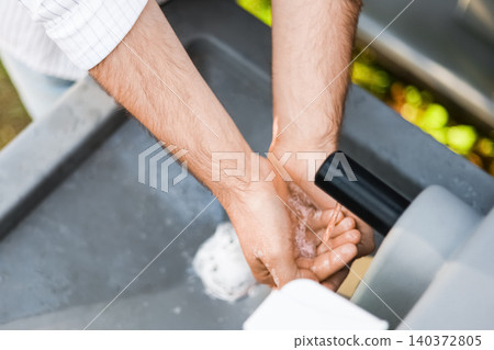 Close-up of a man washing his hands under running water at an outdoor portable sink station, focusing on personal hygiene, cleanliness, and sanitation. Close-up of a man washing his hands under running water at an outdoor portable sink station, focusing on personal hygiene, cleanliness, and sanitation. 140372805